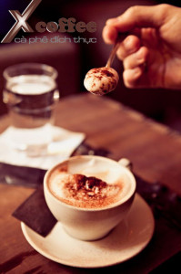 A cup of cappuccino with chocolate frosting and a spoon with milk foam